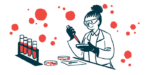 A scientist holds a dropper filled with red liquid over a petri dish near a rack containing vials.