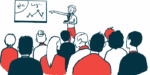 A person in red pants points to a graph as a large, seated audience watches.