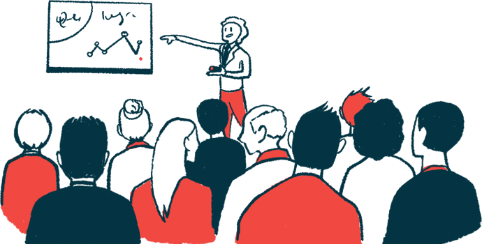 A person in red pants points to a graph as a large, seated audience watches.