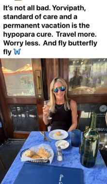 A screenshot of a Facebook post shows a photo of a woman sitting at a table on what appears to be a restaurant patio. She had blond hair, is wearing sunglasses and a black top, and is holding up her drink in a "cheers" gesture. The text above the photo reads: "It's not all bad. Yorvipath, standard of care and a permanent vacation is the hypopara cure. Travel more. Worry less. And fly butterfly fly."