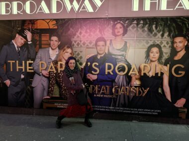 A woman strikes a pose in front of a large Broadway theater sign for "The Great Gatsby."