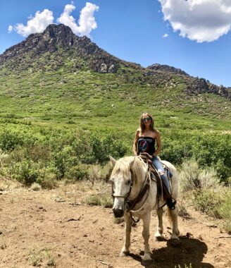 A woman is shown outside on horseback