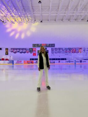 A woman pauses in the middle of an indoor ice rink to smile for a photo.